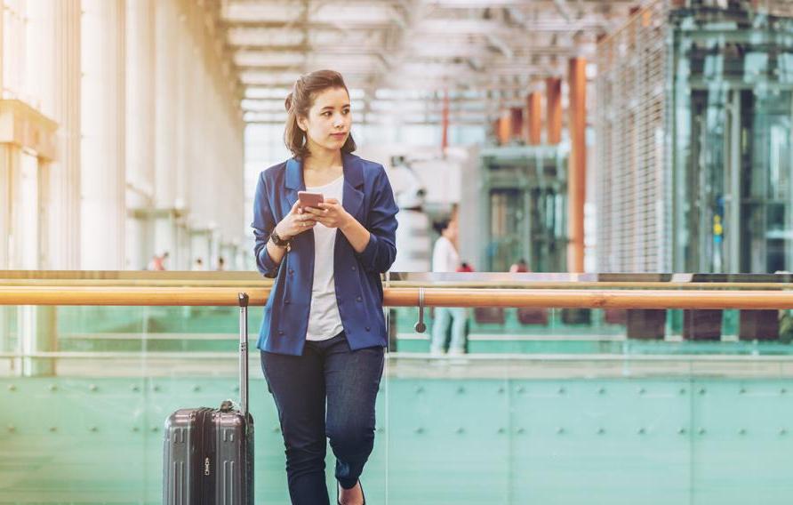 Stock image of business woman holding a cell phone in an airport with suitcase