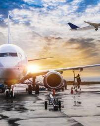 Stock image of an airplane loading with another plane taking off into the sunset 